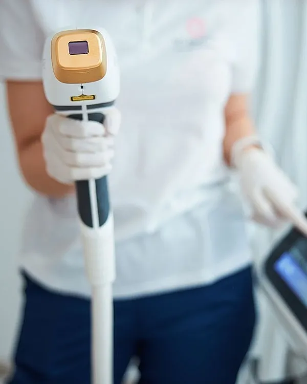 Behandlerin in Handschuhen hält das Handstück des Diodenlasers, daneben der Bildschirm des Geräts