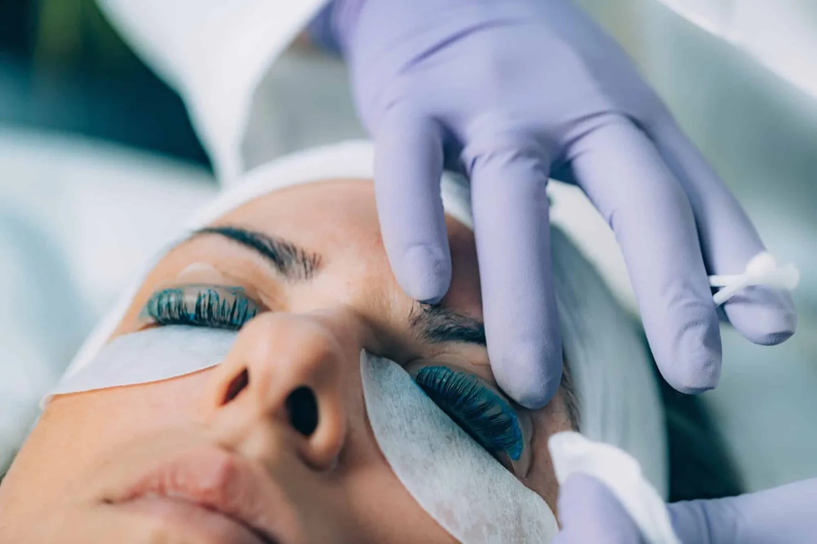 Kosmetikerin mit Handschuhen hebt die Wimpern einer liegenden Kundin an