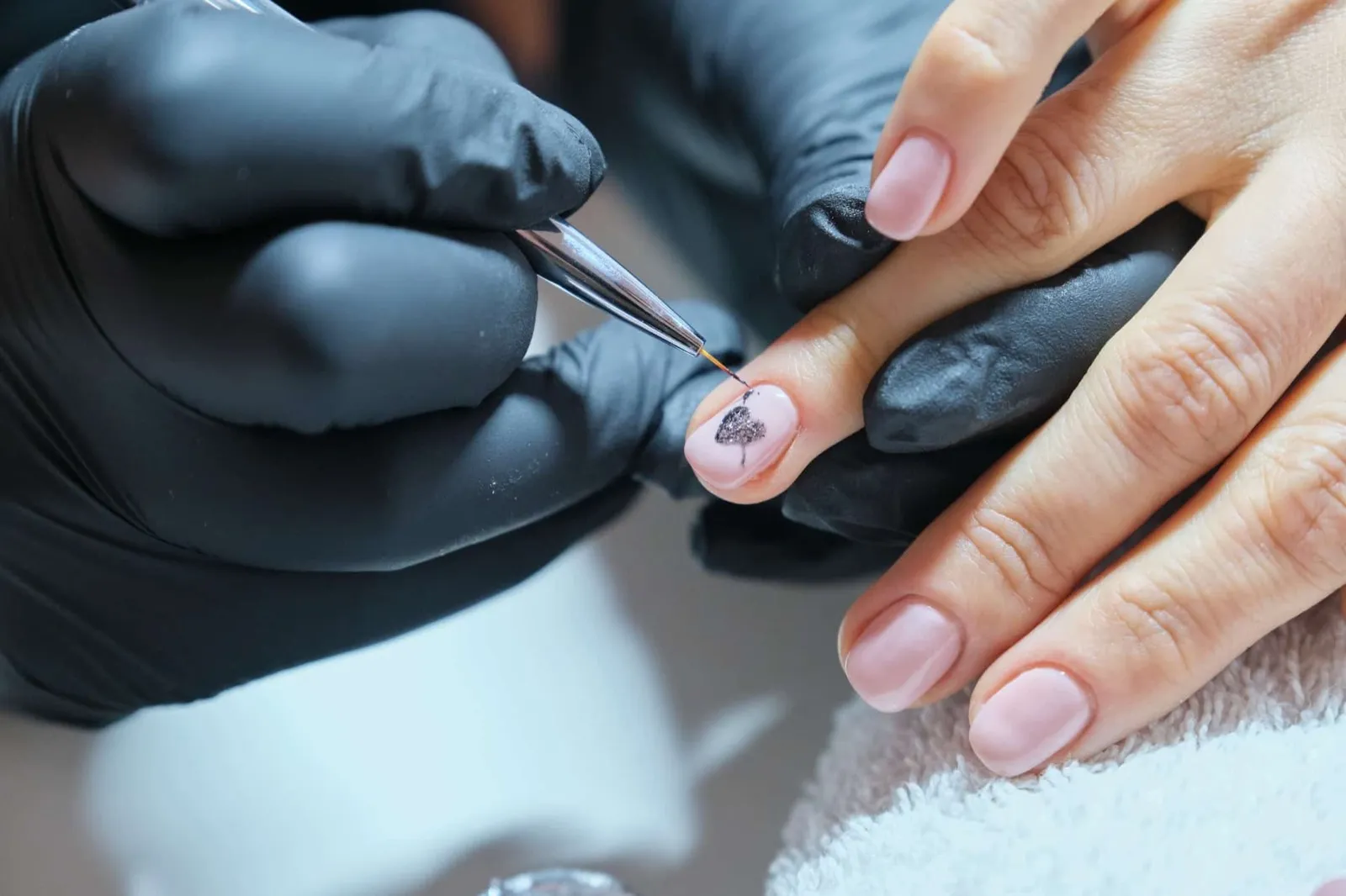 Kosmetikerin malt mit einem feinen Pinsel ein Muster auf einen Fingernagel